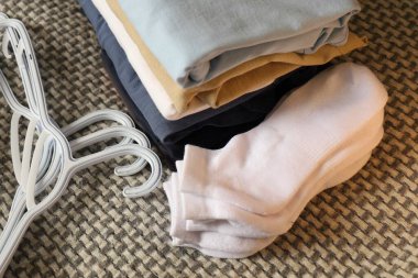 Katlanmış giysiler, beyaz çoraplar ve halının üzerindeki plastik askılar gardırobu düzenlemeye hazırlanıyor.