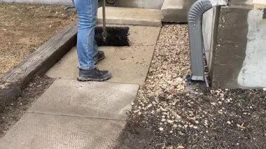 Güneşli bir günde kaldırım kenarındaki kum ve tozu süpüren kişi.