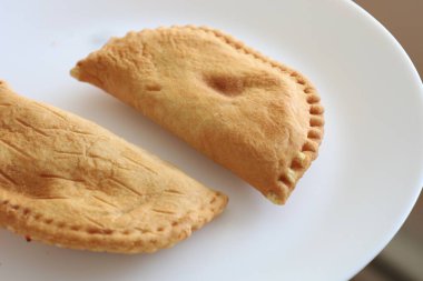 Beyaz tabakta çıtır çıtır kızarmış iki altın sarısı hamur işi. Yarım ay şeklinde ve pişmiş.