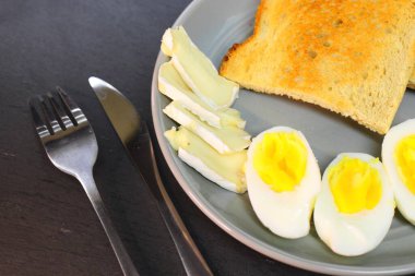 Kızarmış ekmek, kaynamış yumurta kremalı yumurta ve gri tabakta bir dilim yumuşak peynir..