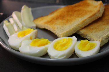 Kızarmış ekmek, kaynamış yumurta kremalı yumurta ve gri tabakta bir dilim yumuşak peynir..