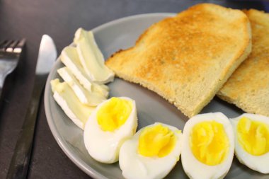 Kızarmış ekmek, kaynamış yumurta kremalı yumurta ve gri tabakta bir dilim yumuşak peynir..