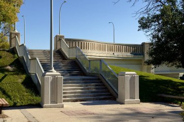 Güneşli bir günde parkta yakalanan, yaya köprüsüne çıkan beyaz parmaklıklı beton merdiven..