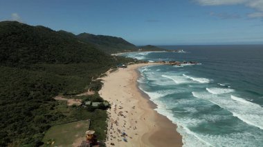 Sahil şeridinin yukarısında, el değmemiş bir plajın çarpıcı hava manzarasıyla süzül. Kristal berraklığında sular, yumuşak, altın gibi kumlarla buluşur ve mavi ile beyazın mükemmel bir karışımını yaratır. Ritmik dalgalardan sakin kıyılara büyüleyici bir manzara..