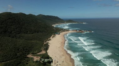 Sahil şeridinin yukarısında, el değmemiş bir plajın çarpıcı hava manzarasıyla süzül. Kristal berraklığında sular, yumuşak, altın gibi kumlarla buluşur ve mavi ile beyazın mükemmel bir karışımını yaratır. Ritmik dalgalardan sakin kıyılara büyüleyici bir manzara..