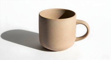 Bu resimde kırsal, benekli bir seramik bardak beyaz bir yüzeyde sergileniyor. Yumuşak bir gölge, sunduğu basit zevki ve sessizliği ima eder..