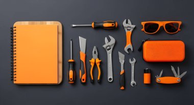 Bir portakal merkezli araçlar koleksiyonu ve koyu bir arkaplan üzerine kurulmuş eşleşen bir defter. Güneş gözlüğü ve DIY veya onarım için çeşitli el aletleri içerir.
