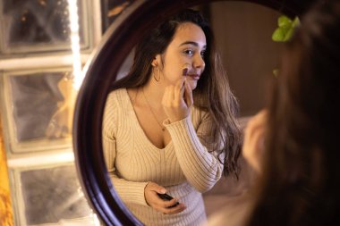 Kız aynanın önünde makyaj yapıyor.