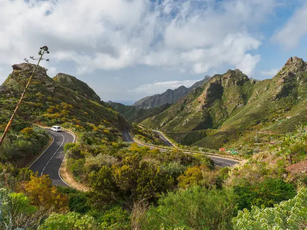 stock image A scenic mountain road winds through lush green hills, offering a picturesque journey through nature.