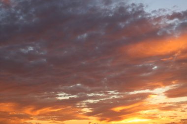 Çarpıcı bir günbatımı gökyüzü canlı turuncu, pembe ve mor renklerle parıldıyor, dramatik bulutlar nefes kesici sahneye derinlik ve doku katıyor. Özgeçmiş ve doğa temalı projeler için mükemmel..