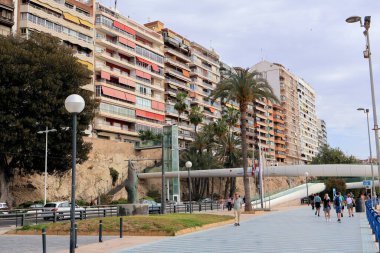 Alicante, İspanya - 2024.04.27. - Passarela del Postiguet - renkli apartman binalarının gezinti güvertesi oluşturduğu canlı bir şehir manzarası. Palmiye ağaçları ve yaya yolları davetkar bir atmosfer yaratırken, insanlar boş boş geziniyor..