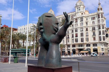 Alicante, İspanya - 2024.04.27. Homenaje a las Hogueras de San Juan - geniş, soyut bronz bir heykel uzanan, tarihi binaların ve palmiye ağaçlarının kentsel zeminine bakan, dağınık bulutlu mavi bir gökyüzünün altında.