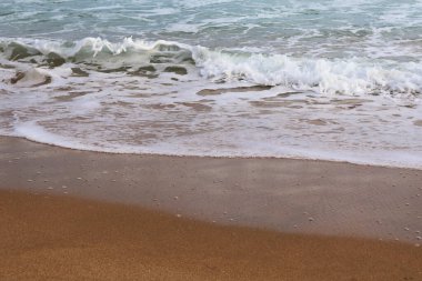 Yumuşak okyanus dalgalarının kumlu sahili okşayışının yakın görüntüsü. Köpüklü su, pürüzsüz kuma karşı yumuşak bir kontrastlık yaratır. Huzurlu bir sahil ortamının huzurlu özünü yakalar..