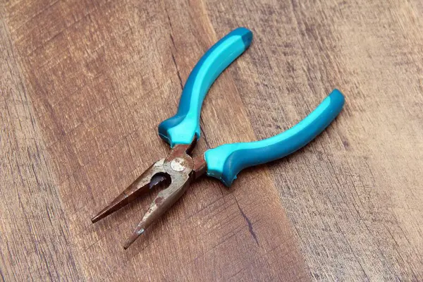 İki ton mavi saplı uzun burun pensesi ahşap bir arka plan oluşturur.