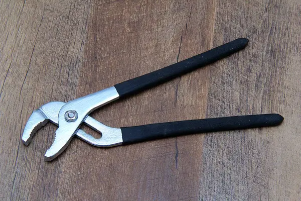 Su pompası pensesi ahşap efekt arka planına karşı siyah kabzalı.