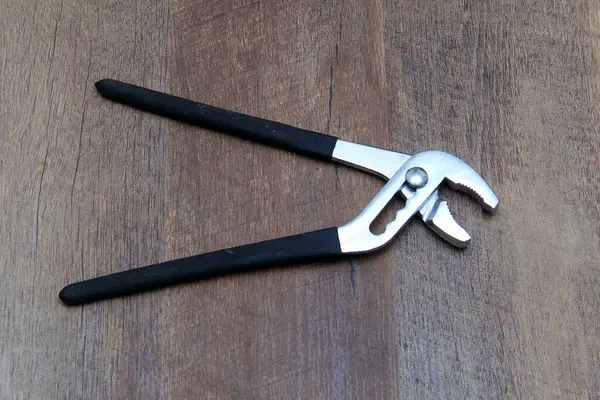 Su pompası pensesi ahşap efekt arka planına karşı siyah kabzalı.