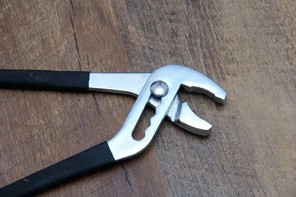 Su pompası pensesi ahşap efekt arka planına karşı siyah kabzalı.