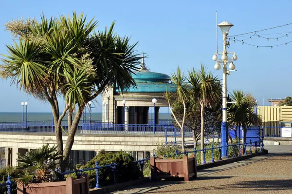 Güneşli bir günde, Eastbourne Orkestra Standı ağaçlarla ve ön planda geziniyor.