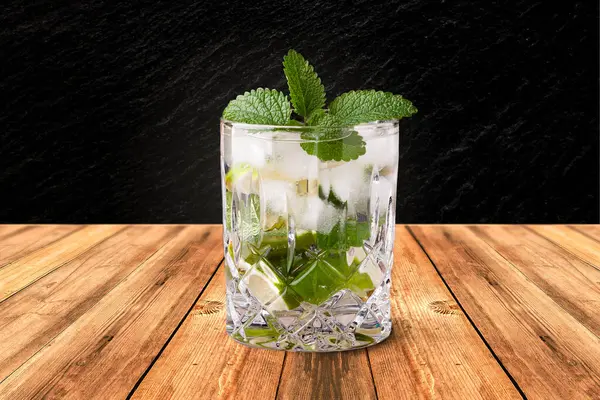 Ayrı bir mojito, siyah arka planı olan ahşap bir masada duruyor.