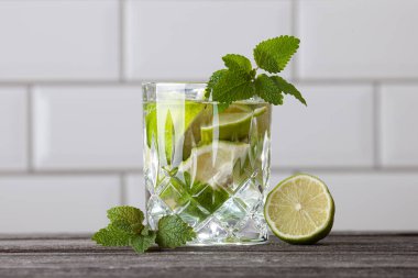 Ahşap bir masada orijinal Caipirinha kokteyli. Arka planda beyaz fayanslar var. Limon, nane, şeker, rom ve buzlu tarif.