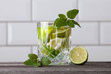 Ahşap bir masada orijinal Caipirinha kokteyli. Arka planda beyaz fayanslar var. Limon, nane, şeker, rom ve buzlu tarif.