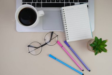 Bir fincan kahve, bir dizüstü bilgisayar ve bir defter, krema masasında gözlük. Eğitim, iş ve ofis kavramı. 