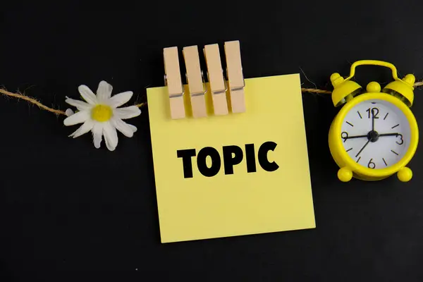 Sarı alarm saatinin yanında siyah zemin üzerinde TOPIC metni olan sarı not defteri bir eğitim ve öğrenme kavramı olarak