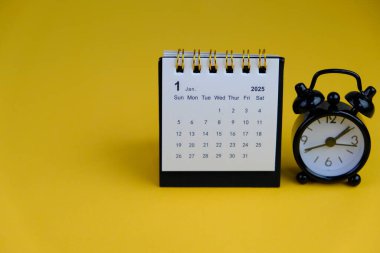 Ocak 2025 tarihli aylık masa takvimi siyah alarmlı ahşap masada..