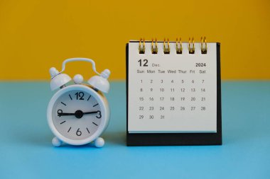 Aralık 2024 tarihli aylık masa takvimi siyah alarmlı ahşap masada..