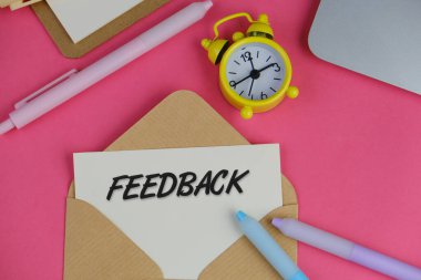 Kağıt ve sarı alarm saatiyle birlikte pembe arkaplandaki beyaz kartın içindeki FEEDback metni