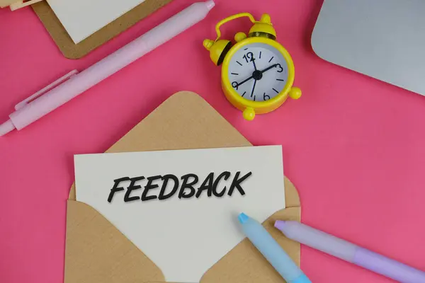 Kağıt ve sarı alarm saatiyle birlikte pembe arkaplandaki beyaz kartın içindeki FEEDback metni
