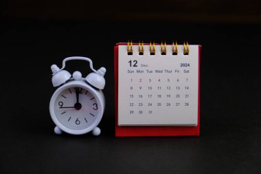 Aralık 2024 tarihli aylık masa takvimi siyah alarmlı ahşap masada..