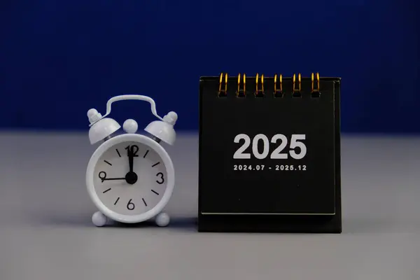 2025 yılının aylık masa takvimi siyah alarmlı ahşap masada..