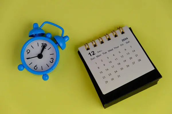 Aralık 2024 tarihli aylık masa takvimi siyah alarmlı ahşap masada..