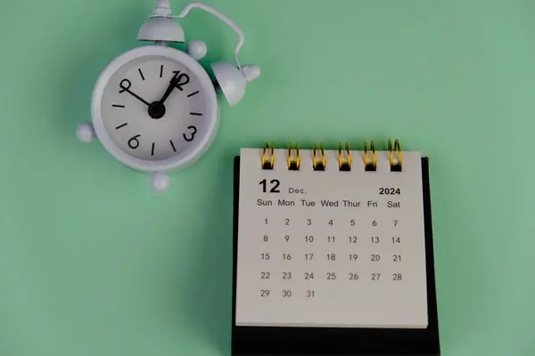 Aralık 2024 tarihli aylık masa takvimi siyah alarmlı ahşap masada..