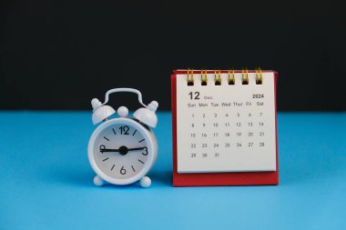 Aralık 2024 tarihli aylık masa takvimi siyah alarmlı ahşap masada..