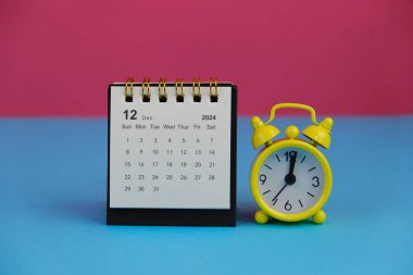 Aralık 2024 tarihli aylık masa takvimi siyah alarmlı ahşap masada..