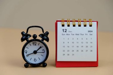 Aralık 2024 tarihli aylık masa takvimi siyah alarmlı ahşap masada..