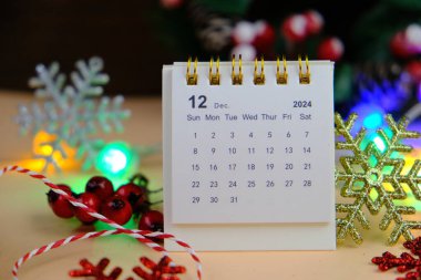 Aralık 2024 tarihli aylık masa takvimi siyah alarmlı ahşap masada..