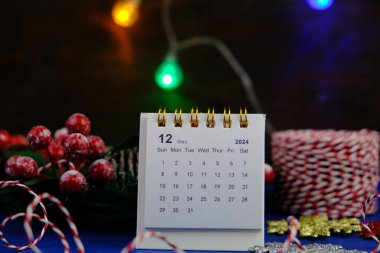 Aralık 2024 tarihli aylık masa takvimi siyah alarmlı ahşap masada..