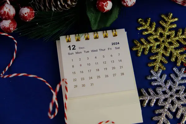 Aralık 2024 tarihli aylık masa takvimi siyah alarmlı ahşap masada..