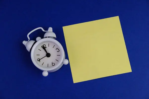 Beyaz alarmlı saat, üzerinde fotokopi alanı konsepti olan sarı etiket. düz mavi arkaplan. 