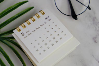 Bir ofis arka planında Mayıs 2025 için aylık masa takvimi. 