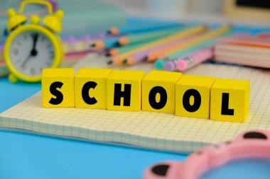 Not defteriyle, kalemlerle ve tahta masaya ataçlarla okula dönüş kavramı. Mavi arkaplan üzerindeki Okulun metni