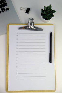 Günlük, kalem, dizüstü bilgisayar, kahve fincanı ve gri arka planda dekor bitkisi olan boş bir çalışma alanı. Üst manzara, düz yatış. kontrol listesi konsepti