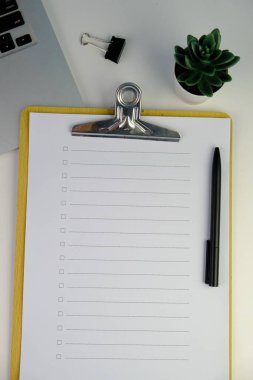 Günlük, kalem, dizüstü bilgisayar, kahve fincanı ve gri arka planda dekor bitkisi olan boş bir çalışma alanı. Üst manzara, düz yatış. kontrol listesi konsepti