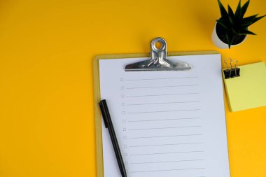 Günlük, kalem, dizüstü bilgisayar ve gri arka planda dekor bitkisi olan boş bir sayfası olan minimum çalışma alanı. Üst manzara, düz yatış. Kontrol listesi konsepti. 