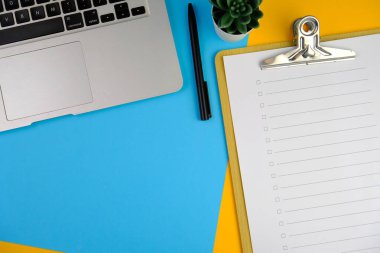 Günlük, kalem, dizüstü bilgisayar, kahve fincanı ve gri arka planda dekor bitkisi olan boş bir çalışma alanı. Üst manzara, düz yatış. kontrol listesi konsepti