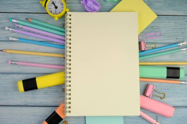 Canlı sarı bir arka planda okul malzemeleri çeşitliliğinin üst görüntüsü. Bu resim renkli kalemler, defterler, makas, silgi ve ataçları içeriyor, hepsi de okula dönüş için düzgünce yerleştirilmiş.