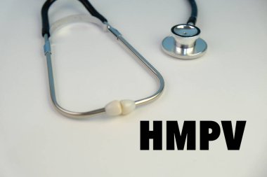 Üzerinde HMPV yazılı bir levha tutan eldiven giymiş bir sağlık görevlisinin resmi. Arka planda steteskop ve tıbbi maske var. İnsan metafnömotorirüsünün (HMPV) belirtileri ciddiyette değişebilir.